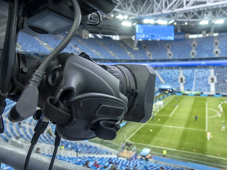 TV Camera Facing Football Pitch in Stadium with Blue Seats